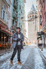 asian man walking around the city of istanbul while holding a camera with galata tower at the background