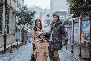Fototapeta premium portrait of asian family wearing warm clothing standing in the middle of snow fall in winter. family travel in turkey