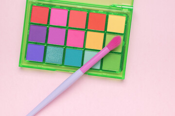 Brush and multi-colored eye shadow on a pink background. Flat lay.