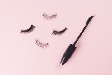 Scattered false eyelashes and a brush on a light pink background.