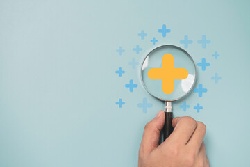 Hand holding magnifier glass with yellow plus sign symbol inside for focus healthcare insurance and offer positive thinking mindset of personal development concept.