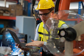 Engineer wearing helmet and hi visible vest working in factory welding robotic automation...