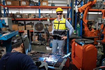Engineer wearing helmet and hi visible vest working in factory hold laptop computer specification...
