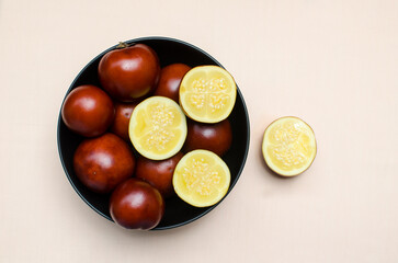 Bowl of ripe cocona fruits displayed on a vibrant peach tablecloth, showcasing tropical freshness and vibrant colors.