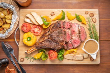 Barbecue Tomahawk Steak on wooden plate.Grilled tomahawk ribeye steak with baked potatoes ,mashroom, roasted sweet peppers and tomato ready to serve. 