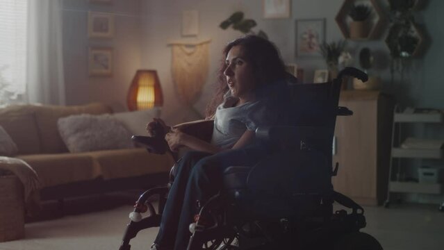 Sad woman with a disability entering the dim room at cozy home and looking at the camera while sitting in an motorized wheelchair