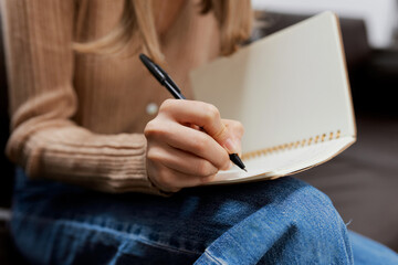 Closeup shot of hand blonde student lady with copybook sitting in sofa couch at modern living room...