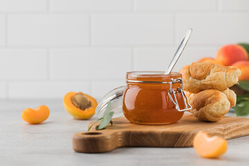 A jar of apricot jam with a spoon inside and with croissants, ripe apricots in a plate. Fruit...