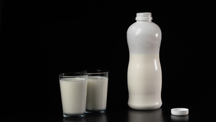 A bottle of kefir or milk with two filled glasses on a black background