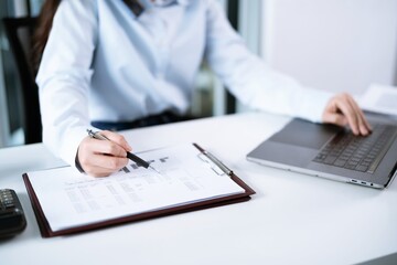 Portrait of  Asian Business woman working from office taking reading and writing notes in note pad working on laptop computer  in her workstation.
