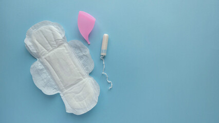Background with feminine hygiene products - disposable pad, tampon and menstrual cup on a solid blue background with space for text