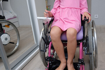Fototapeta na wymiar baby girl in a dress sitting on an electric wheelchair indoors. close-up photo of electric wheelchair joystick