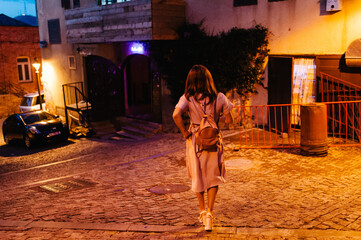 Back view of girl walking on city street at night, in the old town of Tbilisi, the capital of...