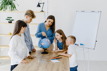 Teacher and children in class are looking at globe, teacher helps explain the lesson to the...