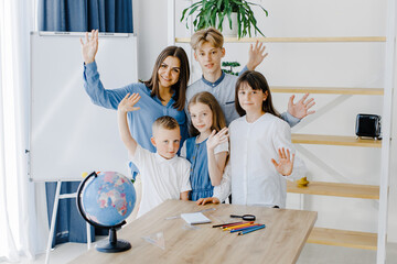 A teacher and schoolchildren of different ages stand in a spacious classroom and smile, looking into the camera.