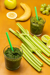 Green smoothie and straw in glasses. Celery stalks and banana on table.