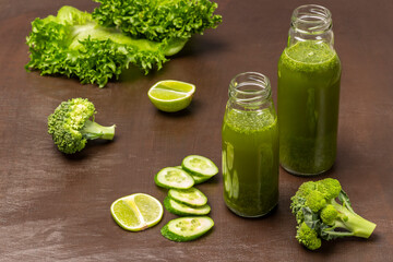 Two green smoothie bottles. Slices of cucumber, lime, broccoli and lettuce on  brown