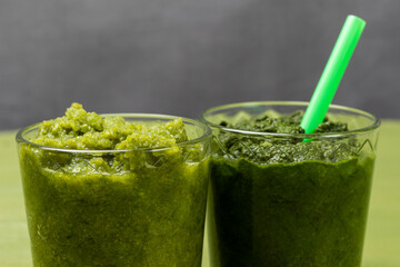 Two glasses with vegetable smoothie. Green straw in a glass.