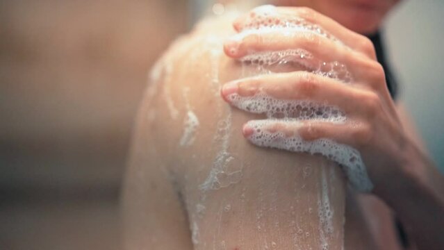 Close-up slow-motion footage of a person's hand washing a shoulder with liquid soap