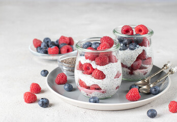 Chia pudding with blueberry and raspberry in two glass jars on light gray background. Healthy food