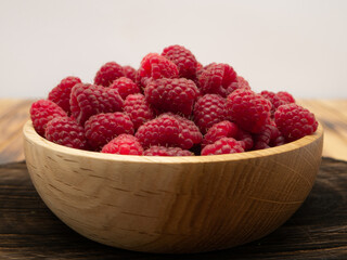 Bowl of fresh fragrant raspberries on rustic wooden background.