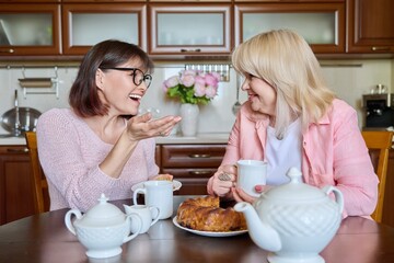Friends two mature women drinking tea with cupcake in kitchen