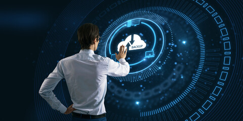 Back view of young businessman pointing at abstract glowing cloud hologram on blurry dark...