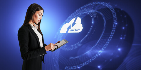 Attractive young european businesswoman holding digital pad with abstract glowing cloud hologram on blurry dark background. Cloud computing, big data backup concept.