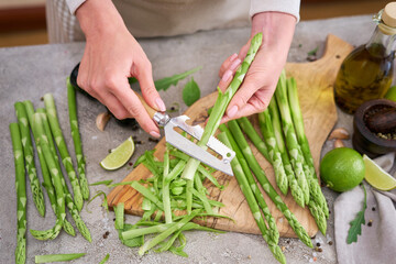 Woman peeling Green Asparagus on wooden cutting board at kitchen table