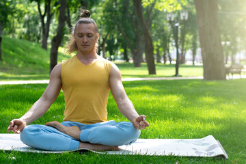 Young man practice yoga in the park. Yoga asanas in city park, sunny day. Concept of meditation,...
