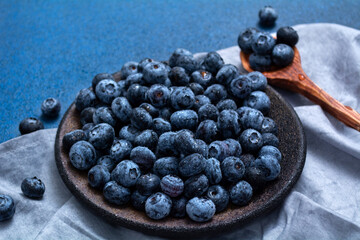 Plate with fresh blueberries on a blue background. Fresh berries and wooden spoon