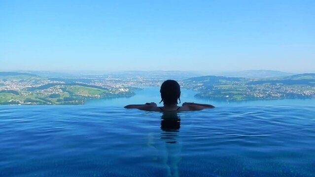 Woman Enjoy Infinity Swimming Pool with View over Mountain and Lake Lucerne in a Sunny Summer Day in Burgenstock, Nidwalden, Switzerland.