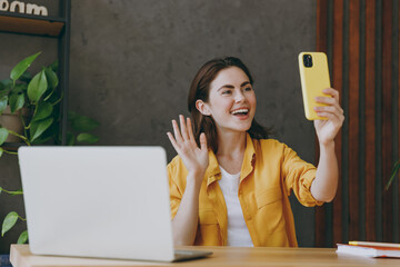 Young employee business woman wear casual yellow shirt waving hand talk by video call doing selfie...