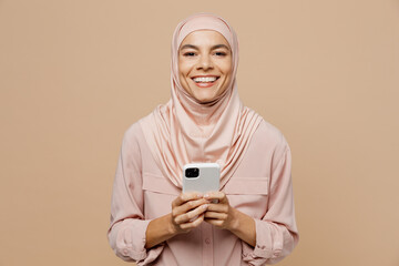 Young arabian asian muslim woman she wear abaya hijab pink clothes hold in hand use mobile cell phone isolated on plain pastel light beige background People uae middle eastern islam religious concept