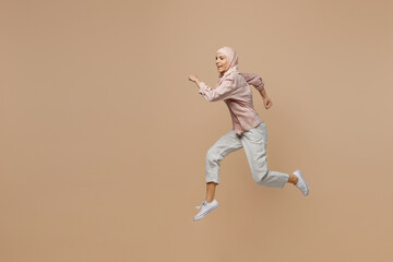 Fototapeta na wymiar Side view full body young arabian asian muslim woman she in abaya hijab pink clothes jump high run hurry up isolated on plain light beige background. People uae middle eastern islam religious concept.