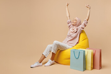 Full body fun young arabian asian muslim woman she wear abaya hijab sit in bag chair near package...