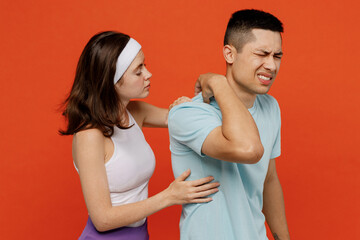 Young sad fitness trainer instructor sporty two man woman in headband t-shirt hold neck suffer from pain spend weekend in home gym isolated on plain orange background Workout sport lifestyle concept.