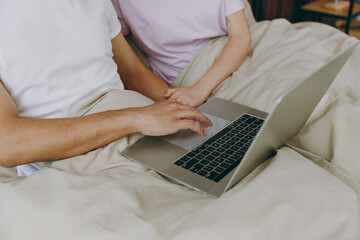 Cropped young couple two family man woman she he wear t-shirt pajama hold use work on laptop pc computer lying in bed rest spend time together in bedroom home in own room hotel. Real estate concept.