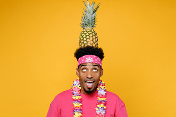 Young surprised shocked man 20s he wear pink t-shirt near hotel pool hold pineapple fruit on head...