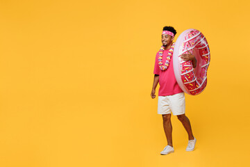 Fototapeta na wymiar Full body young smiling happy man he wear pink t-shirt inflatable donut ring hawaiian lei bandana near hotel pool walking going isolated on plain yellow background. Summer vacation sea rest concept.