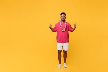 Full body young smiling happy fun man 20s he wear pink t-shirt hawaiian lei bandana near hotel pool showing thumb up like gesture isolated on plain yellow background. Summer vacation sea rest concept.