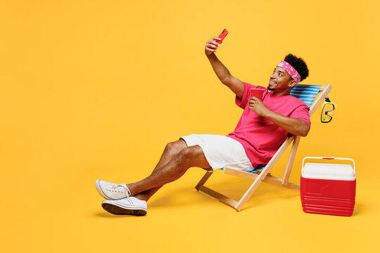 Full body young fun man he wear pink t-shirt bandana near hotel pool doing selfie shot on mobile cell phone drink soda pop water isolated on plain yellow background. Summer vacation sea rest concept.