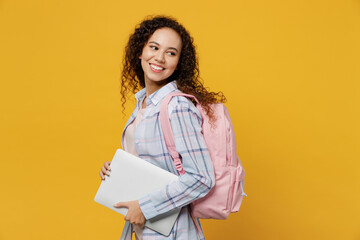 Young fun smart black teen girl student she wear casual clothes backpack bag hold closed laptop pc computer look aside isolated on plain yellow color background. High school university college concept