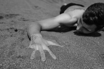 Man lying on his stomach on sand in desert. Selective focus on hand in foreground