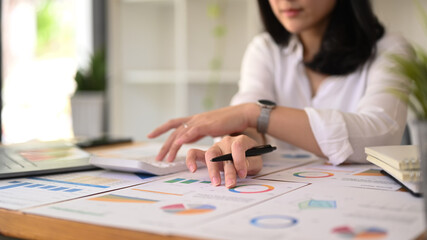 Fototapeta premium Cropped view of female accountant using calculator and examining the numerical data on financial document
