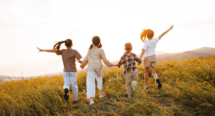 Group of happy joyful school kids boys and girls running with their backs  in field on sunny day