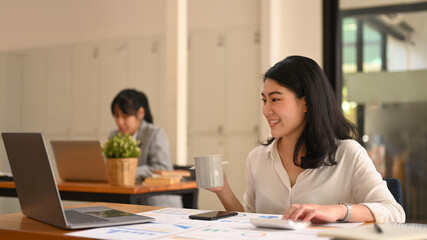 Asian businesswoman using laptop, preparing report analyzing work results at her workplace