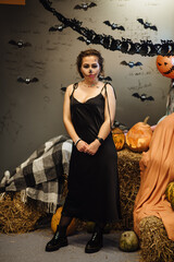 Young sexy gothic girl celebrating Halloween. Portrait of a dead girl among pumpkins with candles. Makeup for Halloween