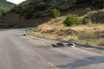 Deep hole on a mountain road. Deformed asphalt surface with potholes melts from heat due to heavy...