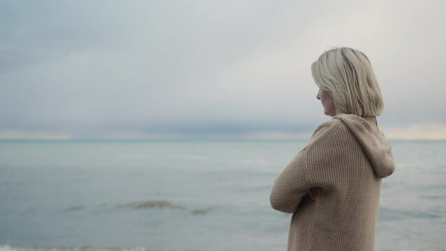 A woman in a warm knitted sweater looks at the sea where the storm begins